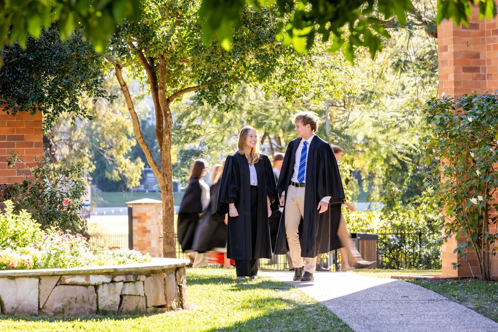 Students in academic gowns walking through the St John's grounds on a sunny day