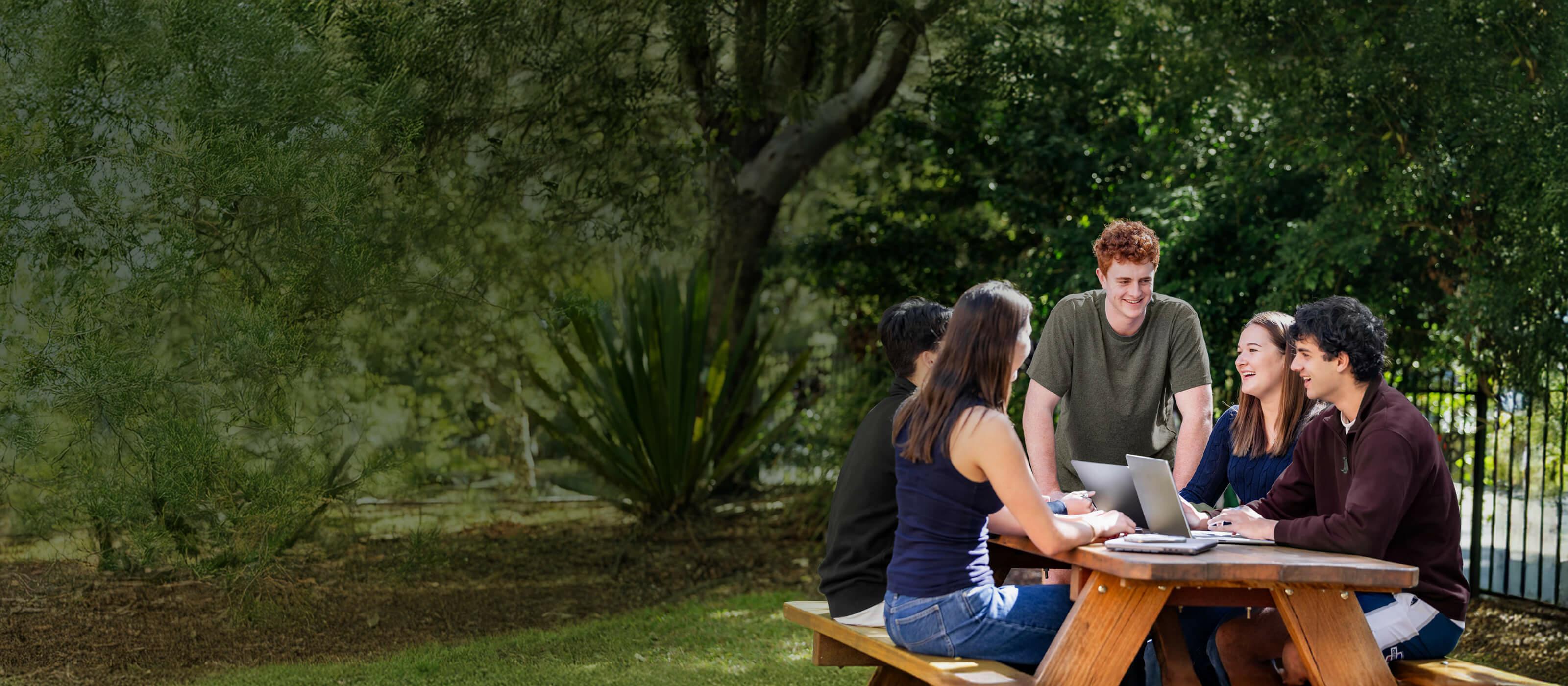 Students around an outdoor table on a beautiful day engaged laughing and smiling